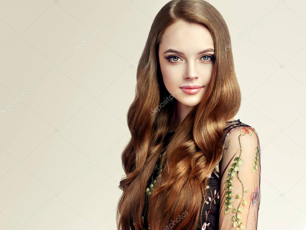 Brunette  girl with long  and   shiny curly hair .  Beautiful  model woman  with curly hairstyle   .Care and beauty of hair