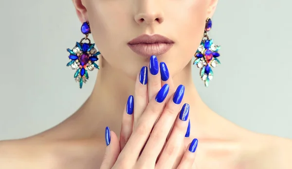 Beautiful model girl with blue manicure on nails . Fashion makeup and cosmetics . Large earrings jewelry .