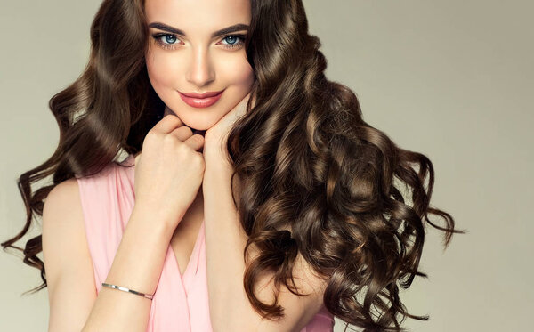 Brunette girl with long , healthy and shiny curly hair . Beautiful model woman with wavy hairstyle .Care and beauty