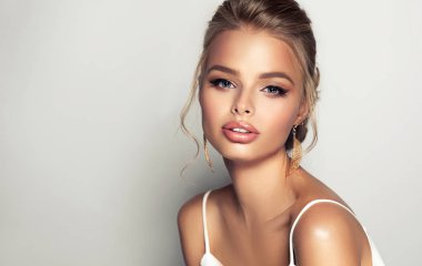 Sarı saçlı güzel bir manken kız. Uzun saçlı bir kadın beyaz bir bluz giyiyor. Moda makyajı ve kozmetik ürünleri. . 