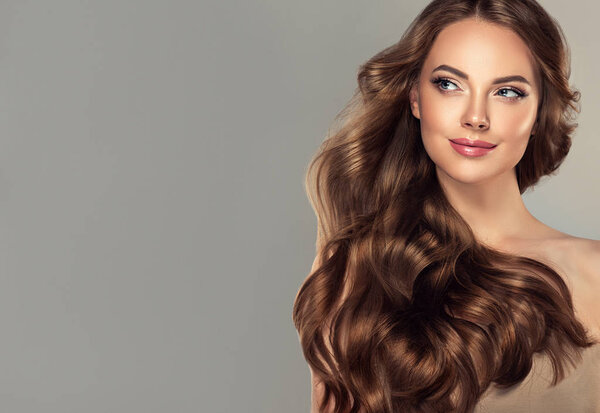 Девушка-брюнетка с длинными и блестящими волнистыми волосами на лбу. Красивая женщина модель с кудрявой прической
 .