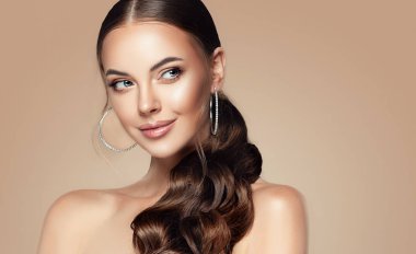 Kafasında kıvrık kuyruğu olan güzel bir kız. Moda takılar takan şık ve şık bir kadın büyük küpeler takıyor. Moda görünüşü, güzellik ve tarz. Doğal makyaj & kolay biçim verme