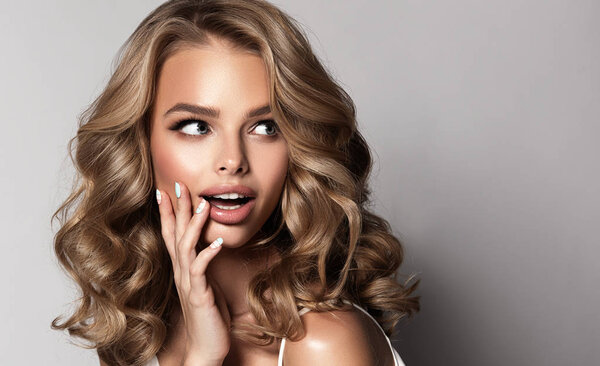 Shocked and surprised girl screaming and looking to the side presenting your product . Beautiful woman with curly hair . Beauty model with wavy hairstyle . Expressive facial expressions