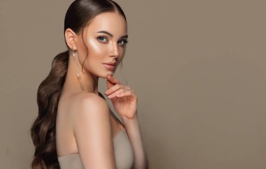 Kafasında kıvrık kuyruğu olan güzel bir kız. Moda takılar takan şık ve şık bir kadın büyük küpeler takıyor. Moda görünüşü, güzellik ve tarz. Doğal makyaj & kolay biçim verme