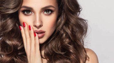 Uzun kıvırcık saçlı güzel esmer model kız. Gülümseyen kadın saç stili dalgalı bukleler. Kırmızı dudaklar ve manikür. Moda, güzellik ve makyaj