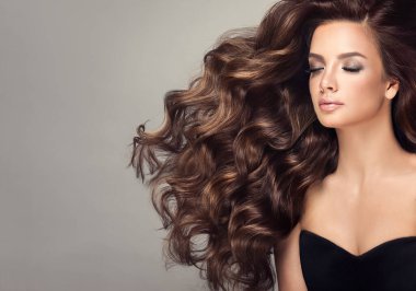 Beauty brunette girl with long and shiny curly hair . Beautiful smiling woman model & wavy hairstyle . Care, treatment and spa