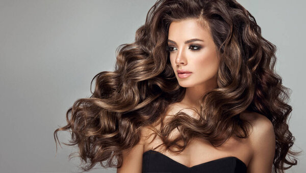 Beauty brunette girl with long and shiny curly hair . Beautiful smiling woman model & wavy hairstyle . Care, treatment and spa