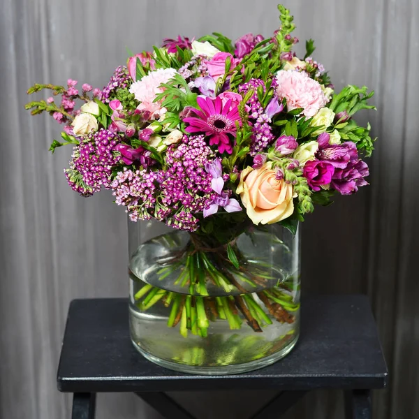 Strauß mit cremefarbenen Rosen und lila Blüten in einer Glasvase — Stockfoto