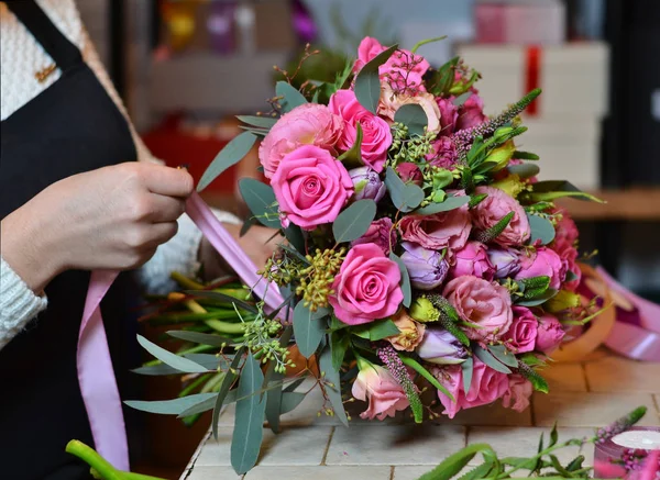 Una mujer hace un ramo de flores en la mesa. Rosas rosadas. Una mujer vendando un — Foto de Stock