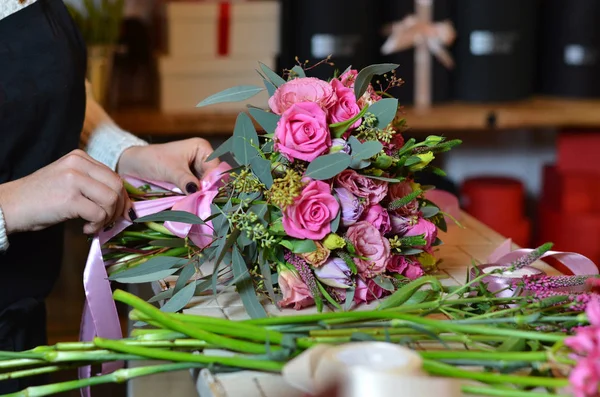Una mujer hace un ramo de flores en la mesa. Rosas rosadas. Una mujer vendando un — Foto de Stock