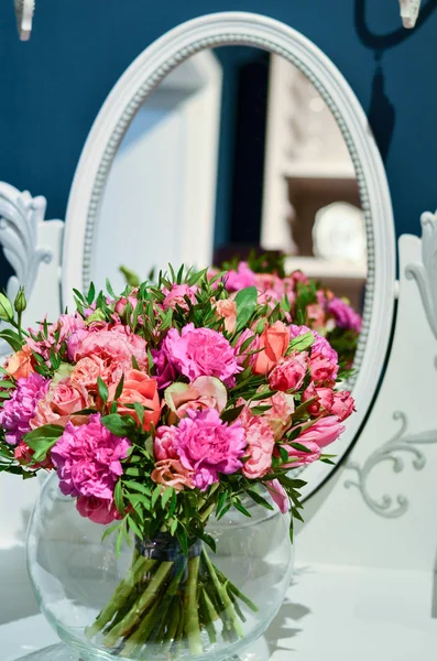 Ramo de rosas en un jarrón de vidrio transparente y circular está sobre la mesa con un espejo . —  Fotos de Stock