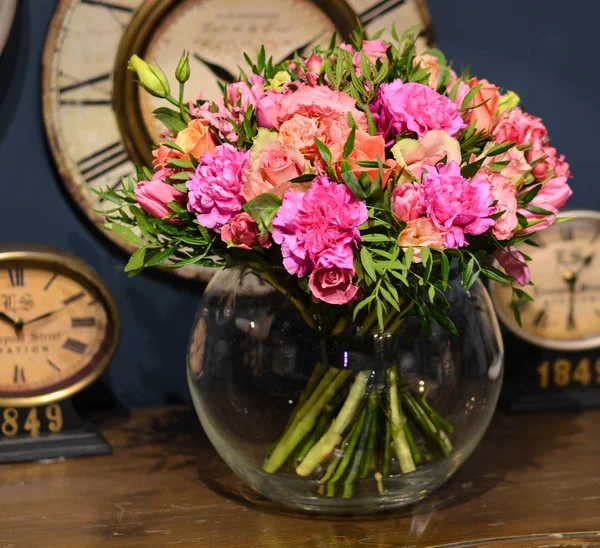 Şeffaf, yuvarlak ahşap bir masa üzerinde duran cam vazo içinde gül buketi