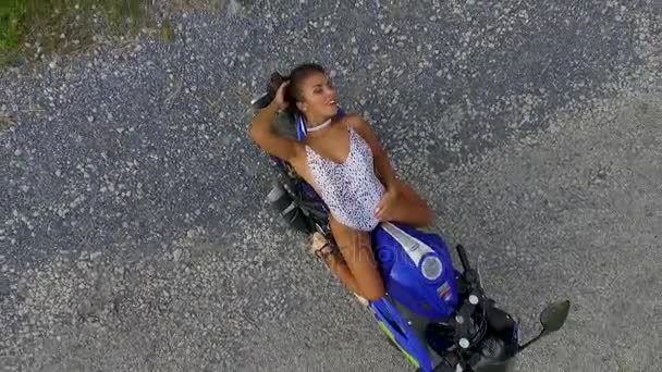 Aerial: Una bella ragazza è in posa e sorride su una moto sportiva. Vista dall'alto . — Video Stock