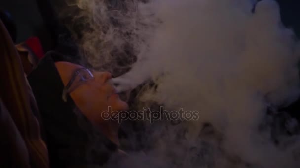 Un hombre en la oscuridad está vapeando e inhala el humo de un cigarrillo electrónico . — Vídeo de stock