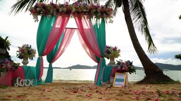 Wunderschöner Hochzeitsbogen mit Blumen am Strand unter Palmen. — Stockvideo