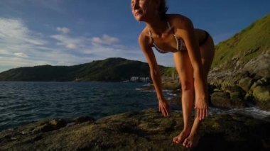 Genç Bayan deniz kenarında kayanın üzerinde yoga yaparken.
