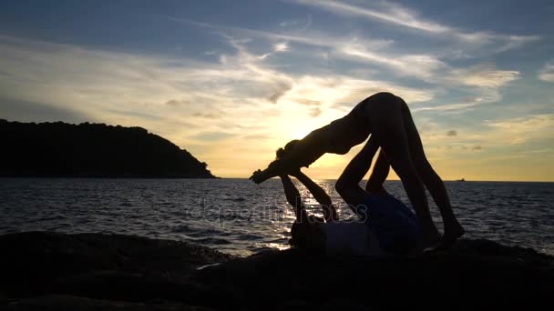 Ζευγάρι κάνει Acro Yoga στο ηλιοβασίλεμα στο βράχο κοντά στη θάλασσα. — Αρχείο Βίντεο