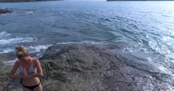 Aérien : Un jeune couple pratique le yoga sur les rochers près de la mer . — Video