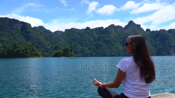 Asijská dívka sedí na molo na jezeře a vypadá do dálky. — Stock video