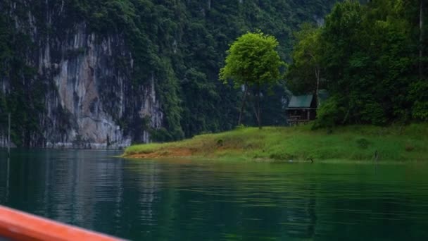 Schießen von einem Boot aus ein kleines Haus auf dem See. Felsen im Hintergrund. — Stockvideo