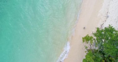 Anteni: Genç bir çift beyaz kum ve turkuaz su ile plajda yürüyor.