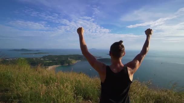 Jeune homme athlétique se tient les mains en l'air sur le bord de la montagne . — Video