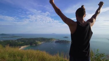 Atletik genç adam elleriyle dağ kenarında ayağa kalkar.