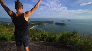 Atletik genç adam elleriyle dağ kenarında ayağa kalkar.