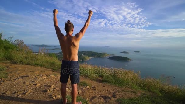 Αθλητική νεαρός άνδρας στέκεται με τα χέρια του επάνω στην άκρη του βουνού. — Αρχείο Βίντεο