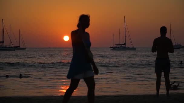 Siluetas de personas caminando por la playa al atardecer. Naves en el horizonte . — Vídeos de Stock