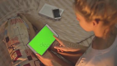Bir kız yatakta oturuyor ve tablet chroma anahtar perde ile kullanma. Swiping.