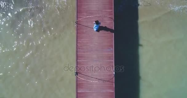 Aerial: Una ragazza asiatica cammina su un molo verso la spiaggia con le palme . — Video Stock