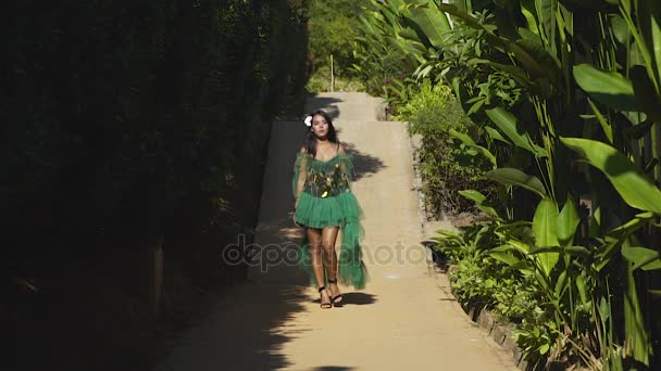 Азиатская модель в зеленом платье выходит на дорогу в тропическом гадене . — стоковое видео