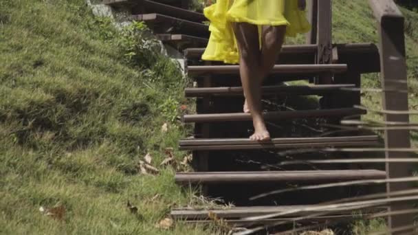 Asian model goes down the stairs in a yellow dress. Near the green grass. — Stock Video