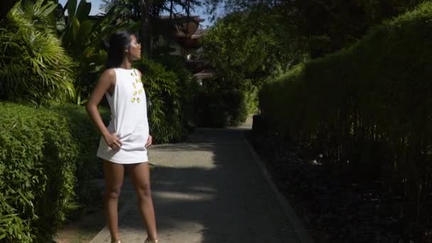 Una joven modelo asiática posando en un vestido corto blanco en un jardín verde . — Vídeo de stock