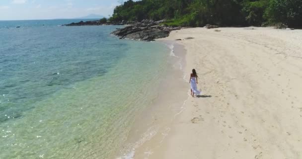 Aerial: Una ragazza vestita di bianco corre lungo la spiaggia in riva al mare . — Video Stock