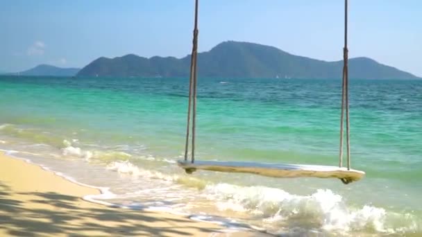 Närbild av en rep gunga hänger på stranden med turkost vatten. — Stockvideo