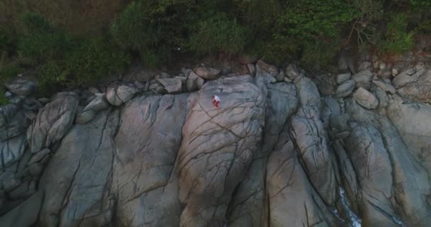 Aérien : Un homme se tient seul sur une falaise et crie émotionnellement en levant les mains 