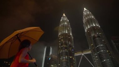 Kuala Lumpur, Malezya 13 Kasım 2019: Kırmızı elbiseli ve şemsiyeli bir kız gece Petronas Kulelerine bakıyor.