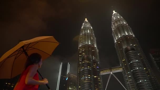 2019 년 11 월 13 일, 말레이시아 쿠알라룸푸르: 밤에 페트로나스 타워를 바라보고 있는 우산을 두른 빨간 드레스를 입은 소녀. — 비디오