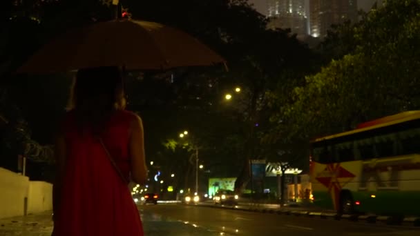 Kuala Lumpur, Malaysia November 13, 2019: En flicka i röd klänning med paraply går nära Petronas Towers på natten. — Stockvideo