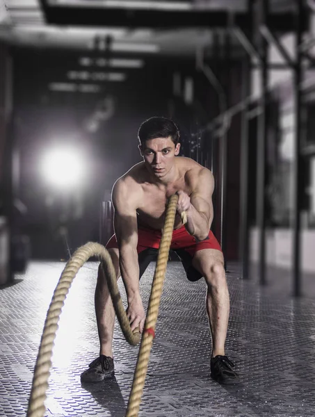 Muscular athlete with battle rope battle ropes exercise in the f