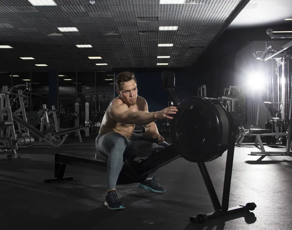 Muscular male athlete on rowing machine in modern fitness center