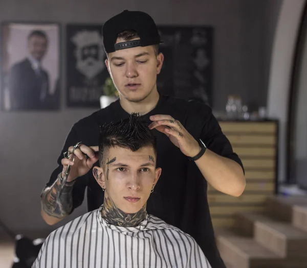 Young man getting haircut by barber while sitting in chair at barbershop