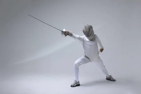 Professional fencer in fencing mask attacking on grey background