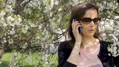 Genç kadın smartphone içinde çiçek açan ağaçlar üzerinde söz