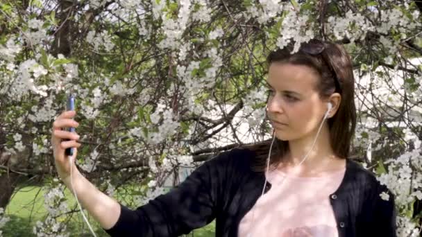 Müzik ve çiçek açan bahçesinde bir selfie alarak kız — Stok video