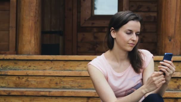 Muchacha atractiva escribe texto en su móvil al aire libre — Vídeo de stock