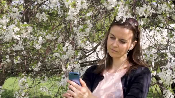 Çiçek açan ağaçlar içindeki genç kız bir selfie alır — Stok video