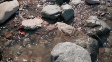 İrili ufaklı taşlar, kırmızı sonbahar yaprakları ve çevrelerindeki çalışan su hızlı akışı kapatın. Ağır çekim